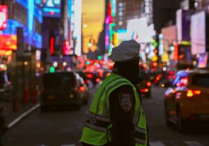 Uniformed police officer in shadow faces away toward city lights
